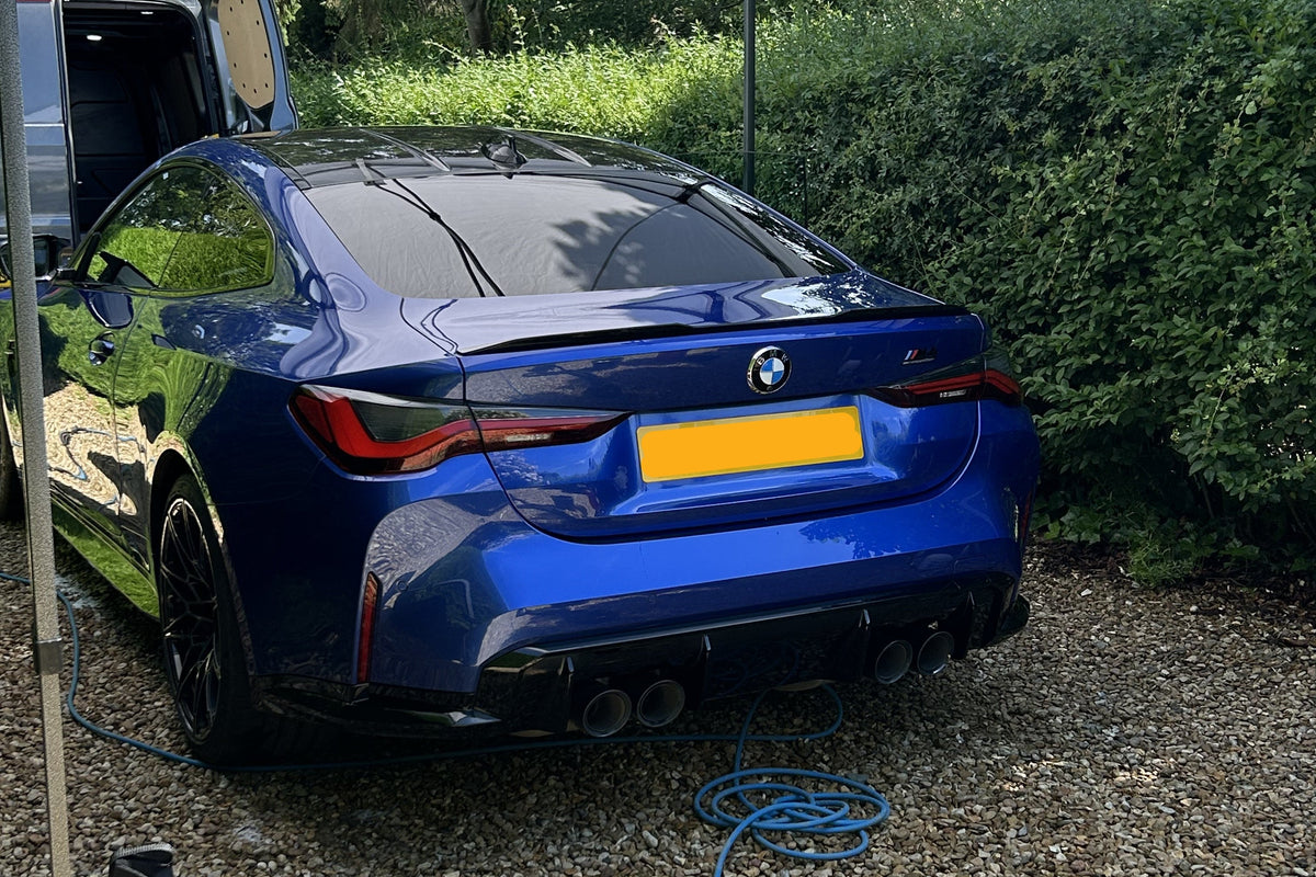 Blue car parked under a white canopy with greenery in the background